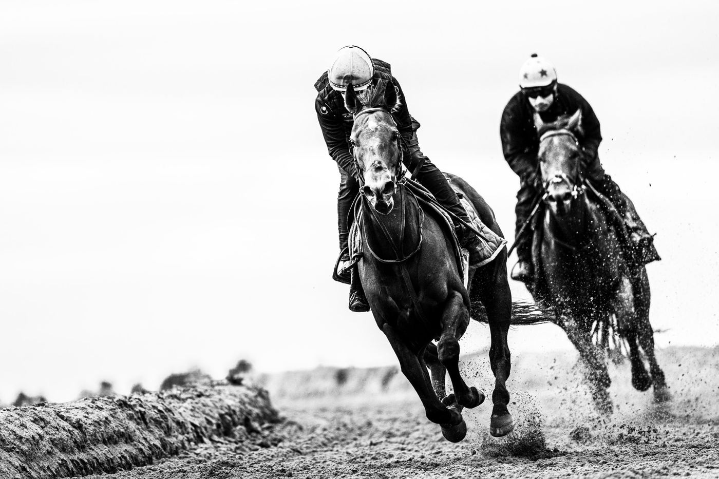 Two racehorses galloping side by side on the sand gallops